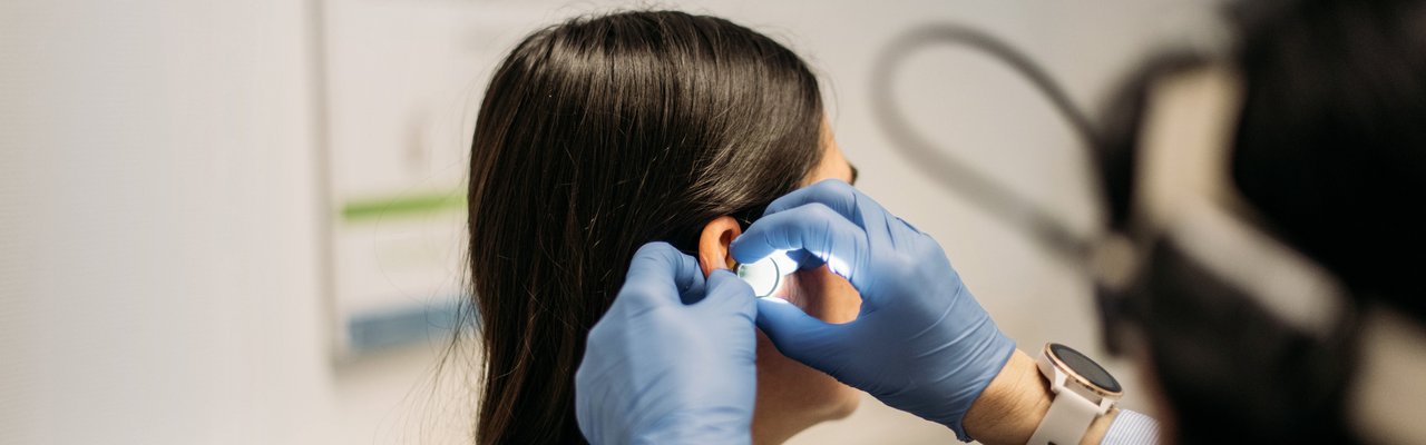 Nahaufnahme eines HNO-Arztes der das Ohr einer Patientin mit einem Otoskop untersucht.