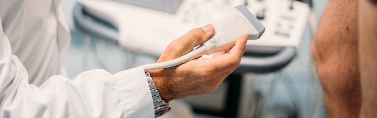 Nahaufnahme der Hand eines Arztes der einen Ultraschallkopf hält, um eine Untersuchung durchzuführen.