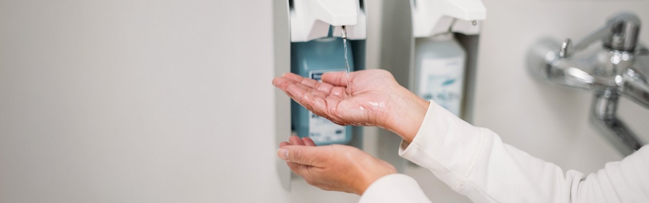 Nahaufnahme der Hände einer Person, die Desinfektionsmittel aus einem berührungslosen Spender in einem Krankenhaus entnimmt.